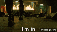 a woman in black boots is standing in front of a burning building and says i 'm in