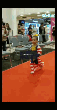 a little girl is running on a red carpet in front of a wells fargo sign