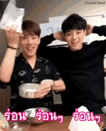 two young men are sitting at a table and one is holding a bag and the other is holding a bowl