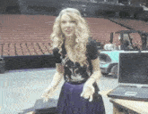 a woman in a black shirt and purple skirt is standing in front of a laptop