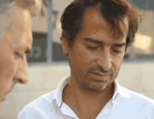 a man in a white shirt with a beard looks down