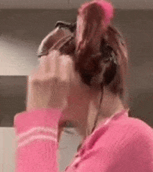 a woman in a pink sweater is wearing headphones and holding a pink object in her hand .