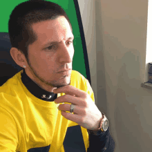 a man wearing a yellow shirt and a black turtleneck has a watch on his wrist