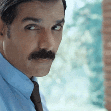 a man with a mustache wearing a blue shirt and brown tie