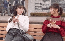 two women sitting on a bench eating ice cream