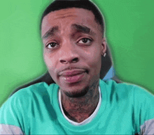 a man with a beard and tattoos is wearing a green shirt and looking at the camera .