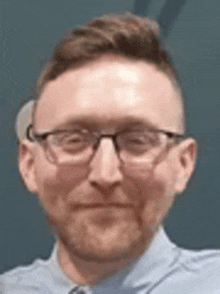 a man wearing glasses and a blue shirt is smiling .