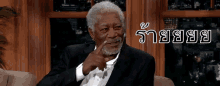 a man in a suit is sitting on a couch with a foreign language written on the bottom right