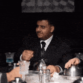 a man in a suit and tie sits at a table with other people