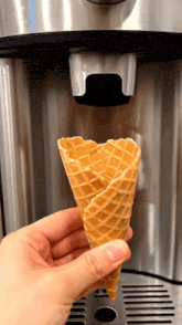 a person is holding a waffle cone in front of a coffee maker