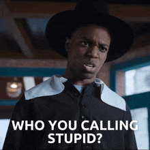 a man in a hat says " who you calling stupid " in front of a window