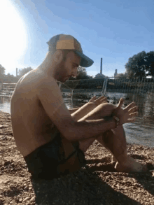 a man in a hat sits on the beach near a body of water