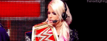 a woman is wearing a headset and holding a wrestling championship belt
