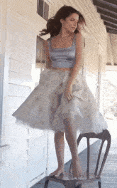 a woman in a crop top and a skirt is standing on a chair