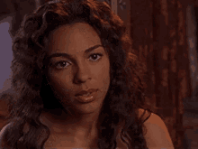 a woman with long curly hair is looking at the camera with a serious look on her face .