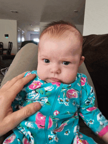 a baby wearing a blue and pink floral onesie looks at the camera