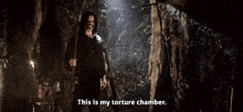 a man standing in a dark cave holding a stick and saying this is my torture chamber