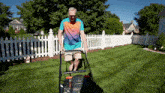 a man is pushing a lawn mower in a yard with a white picket fence