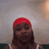 a woman wearing a red headband and a white tank top is looking at the camera .