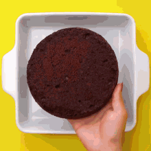 a person is holding a piece of chocolate cake over a white pan