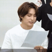 a young man in a white shirt is holding a piece of paper in his hand .