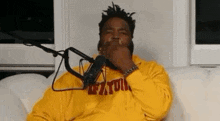 a man in a yellow hoodie is sitting in front of a microphone .