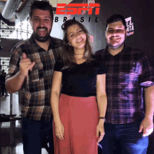 two men and a woman pose for a photo in front of a sign that says espn brasil