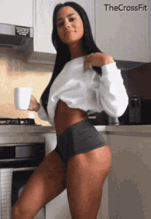 a woman is standing in a kitchen holding a cup of coffee with the crossfit logo in the background