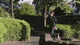 a man in a black jacket is walking down a path surrounded by bushes