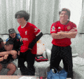 a man wearing a red shirt that says liverpool is standing in a room with other people