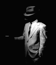 a man in a suit and hat smoking a cigarette in the dark
