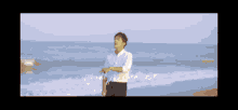 a man in a white shirt is standing on a beach near the ocean