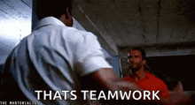 two men are standing next to each other in a room with the words `` that 's teamwork '' written on the bottom .