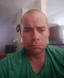 a man with a shaved head is wearing a green shirt and making a sad face .