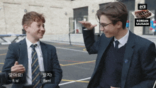 two boys in suits and ties are standing in a parking lot with a sign that says korean sausage above them