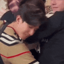 two men are hugging each other in a room . one of the men is wearing a striped shirt .