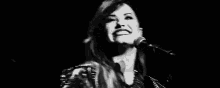 a black and white photo of a woman singing into a microphone on stage .