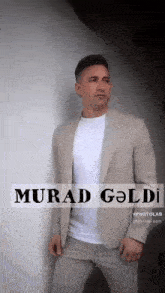 a man in a suit leaning against a wall with murad goldi written in black