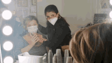 a woman wearing a face mask looks at another woman in front of a mirror