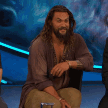 a man with long hair and a beard is sitting on a chair