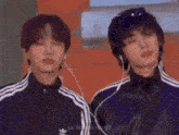 two men wearing headphones and jackets are standing next to each other .