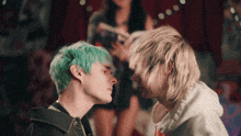 a man with green hair and a man with blonde hair look at each other