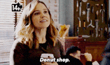 a woman in a donut shop is holding a cup of coffee