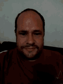 a man with a beard wearing a red shirt looks at the camera