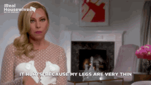 a woman says it hurts because her legs are very thin in front of a fireplace