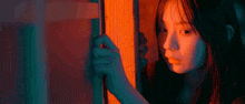 a woman is looking through a glass door with a red and blue light behind her
