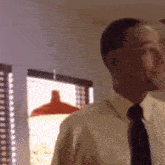 a man in a white shirt and black tie is looking out a window