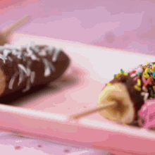 two chocolate covered bananas with sprinkles on a plate