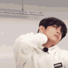a young man in a white hoodie is holding his neck in pain .