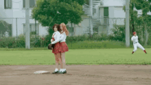 two girls are hugging each other on a baseball field while a baseball player watches .